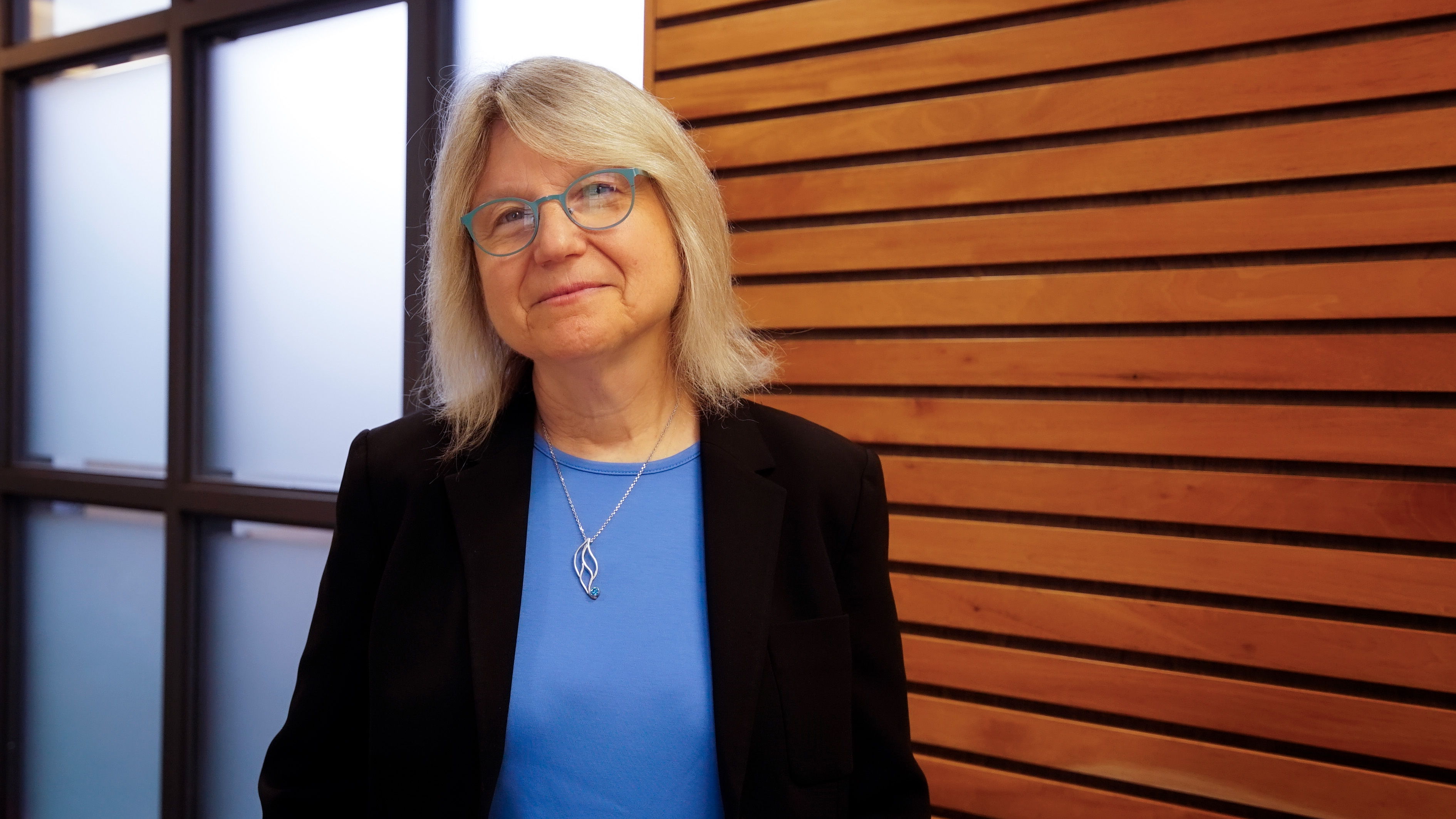Photo of Sally Kornbluth in front of a frosted glass and wood paneling office